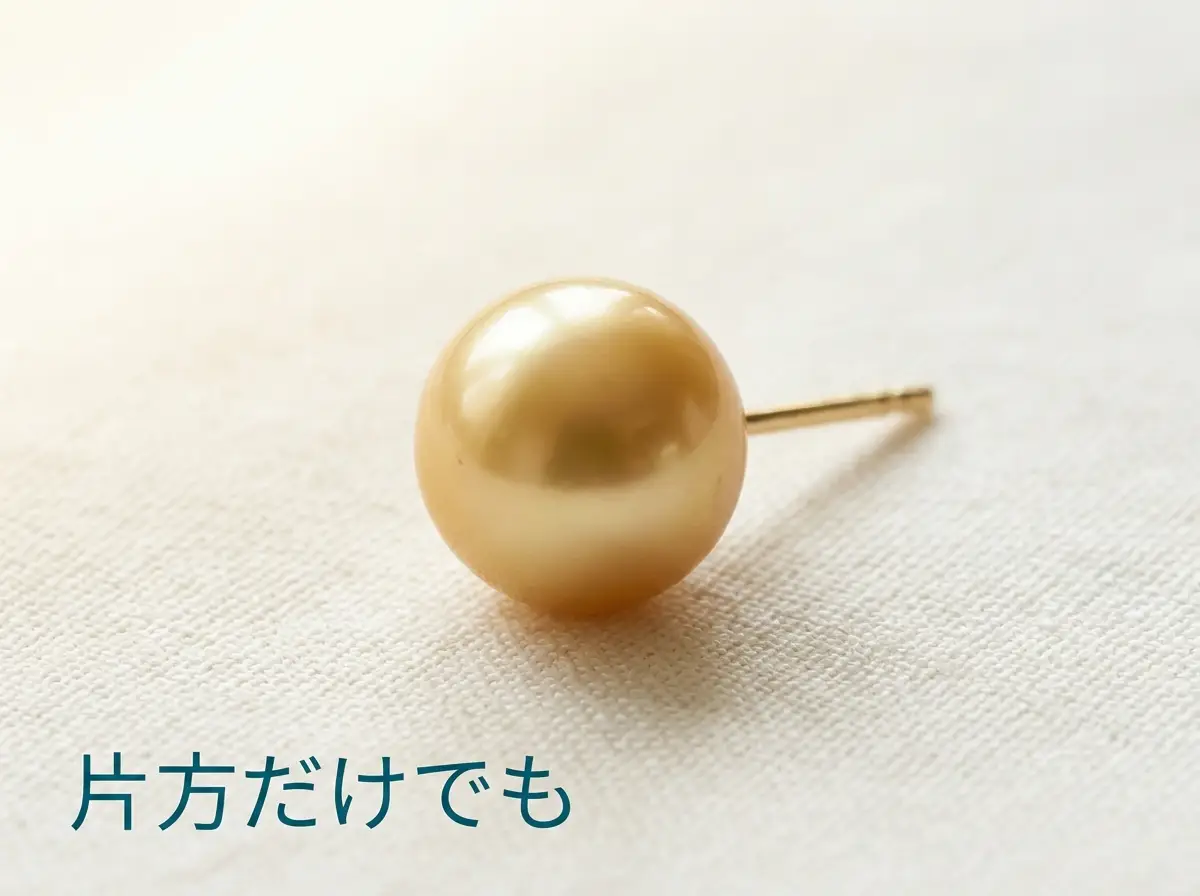 片方だけの金色の真珠のピアスを布の上に置いた写真