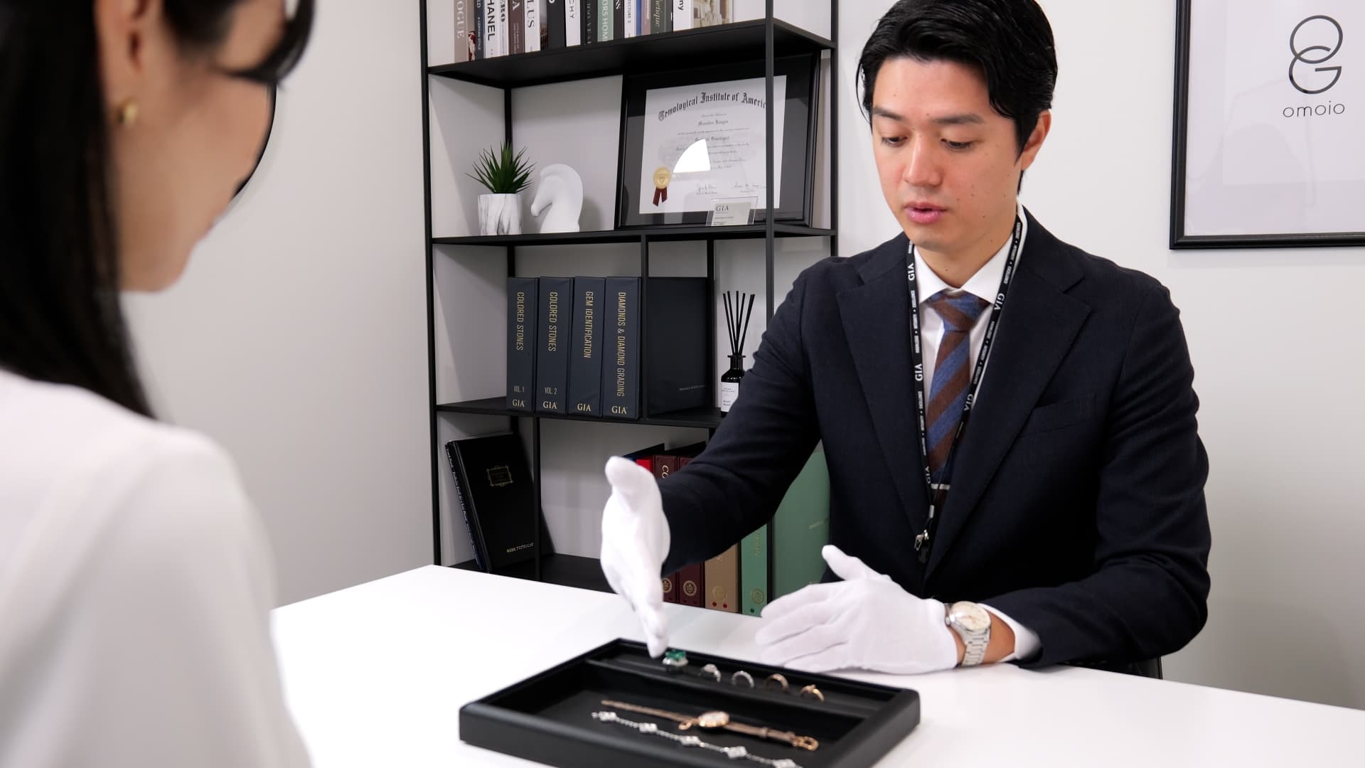 おもいお銀座本店で、白手袋を着けた鑑定士がトレーに並べたリングやブレスレットをお客様の目の前で確認しながら説明している査定の様子